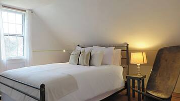 Une chambre à coucher avec un lit, une chaise, une table avec une lampe et une fenêtre.
