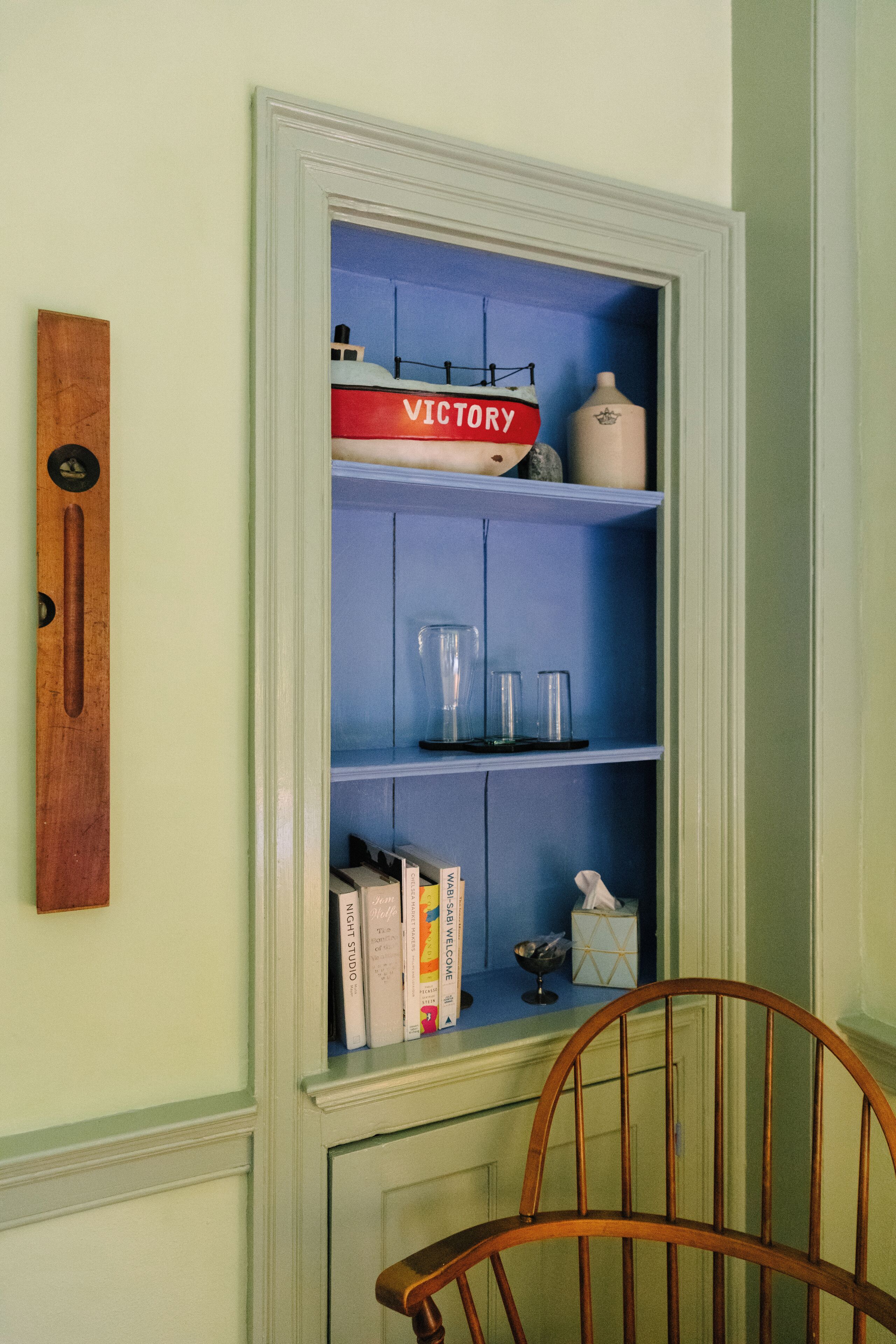 Una habitación con una estantería azul que contiene libros, vasos y un adorno.