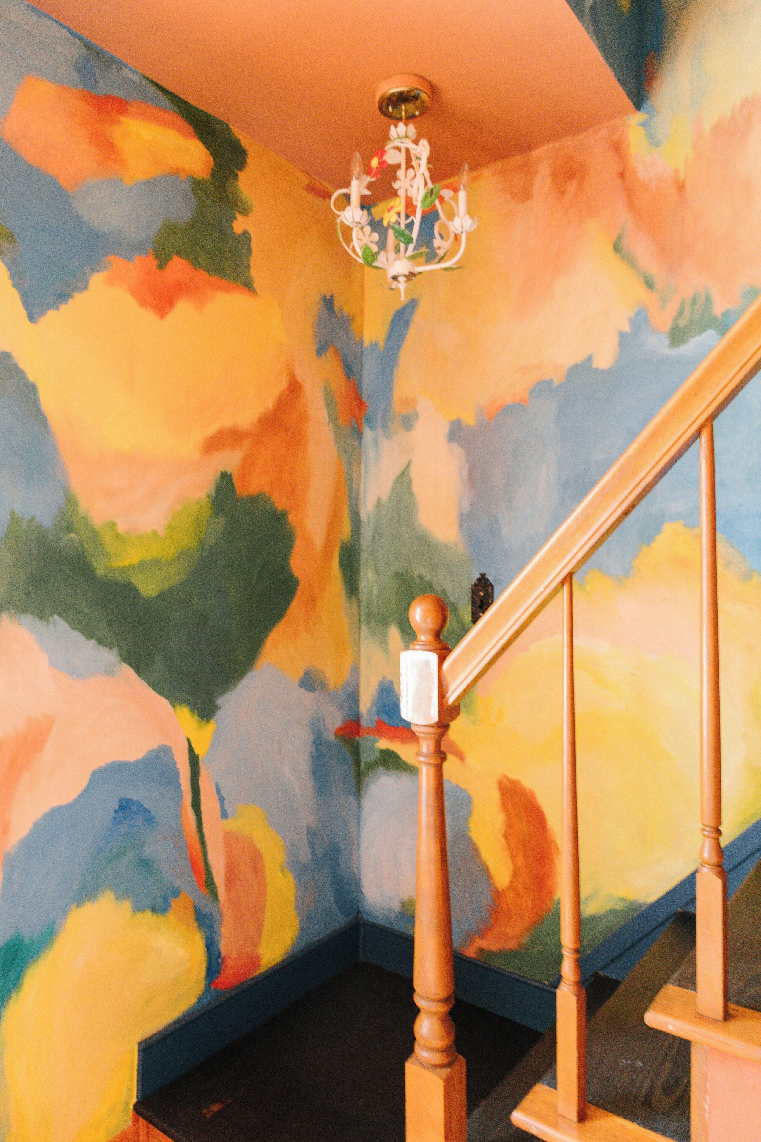 A staircase with a wooden handrail and a colorful abstract mural on the walls.