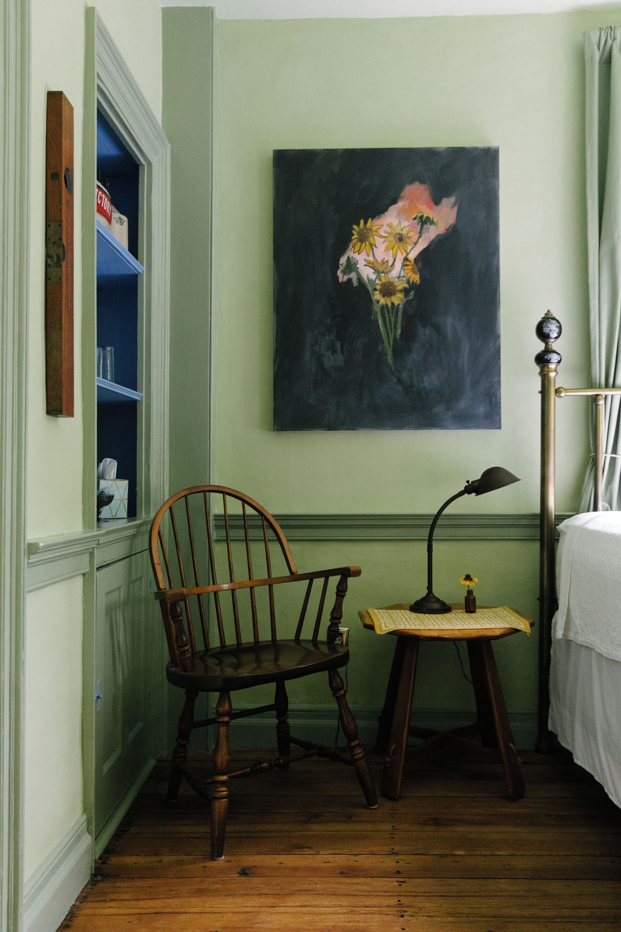 A room with a wooden chair, a small table with a lamp, and a painting on the wall.