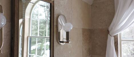 A bathroom with a large mirror, a light fixture, and a window with curtains.