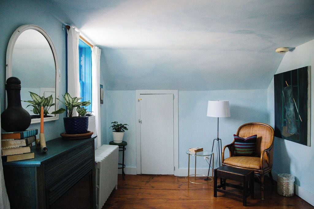 Een kamer met een open haard, een stoel, een klein tafeltje, een lamp en een deur.