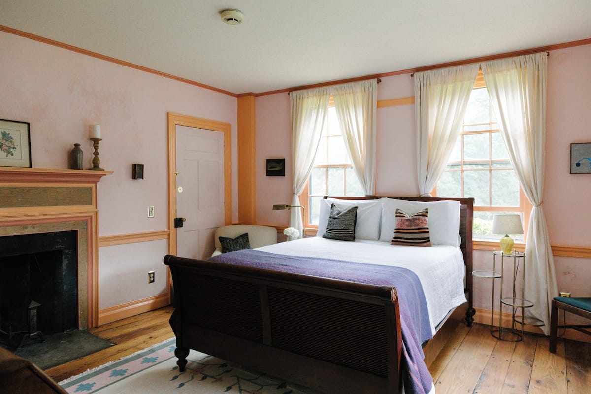 A bedroom with a wooden bed, a fireplace, and a window with curtains.