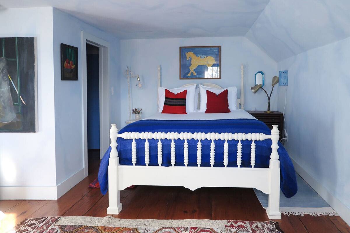 A bedroom with a white bed, blue bedding, and a red and white pillow arrangement.