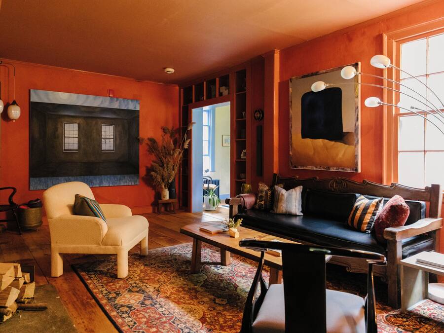 A cozy living room with a sofa, armchair, and coffee table, featuring a large window and a painting on the wall.