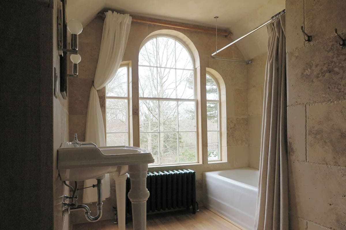 A bathroom with a sink, two windows, a radiator, and a bathtub.