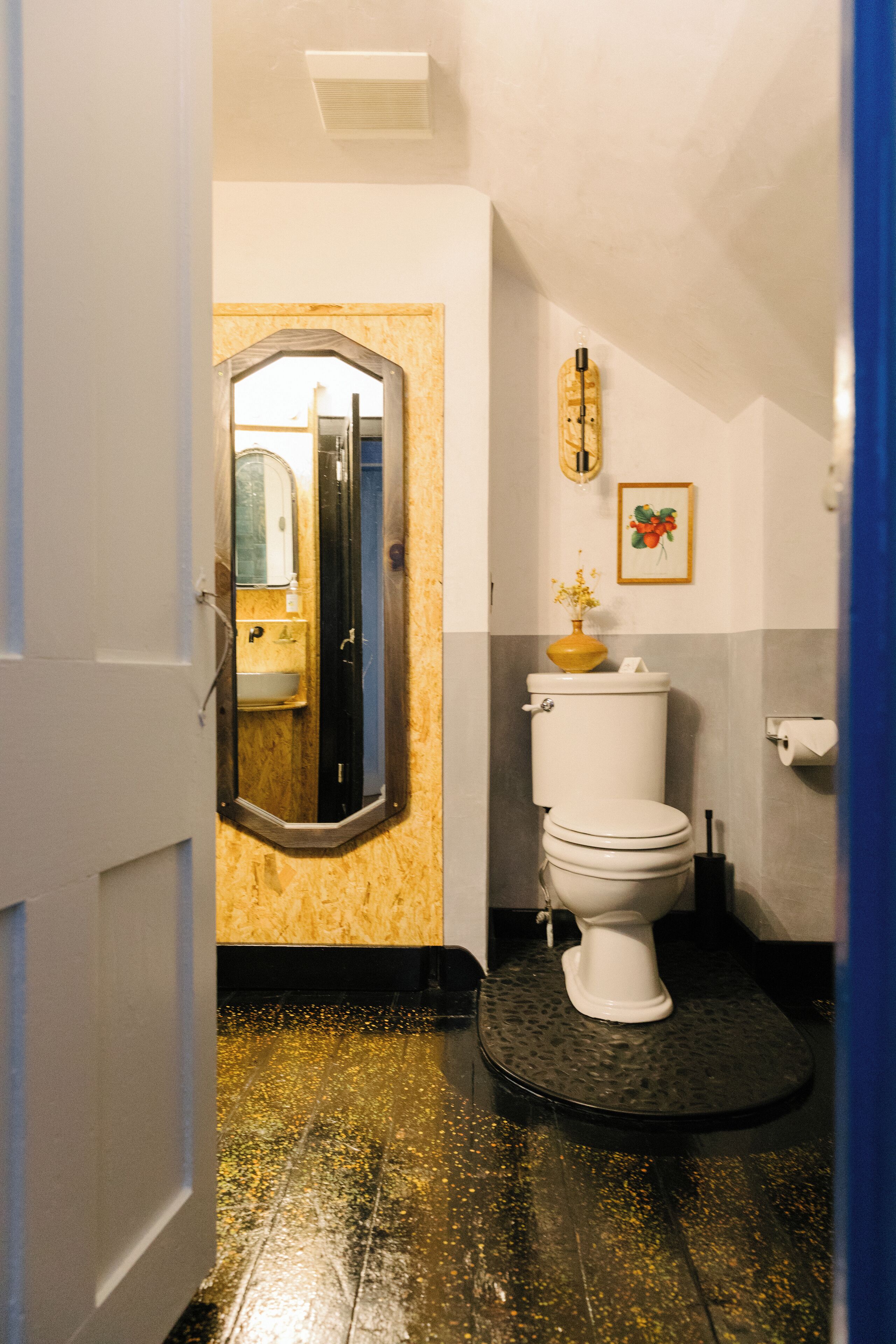 A bathroom with a toilet, sink, mirror, and a decorative vase.
