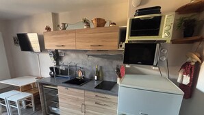 A compact kitchen with wooden cabinets, a built-in microwave, a sink, and a small refrigerator. - Studio Montagne 20 m (Saint-Léger-les-Mélèzes)
