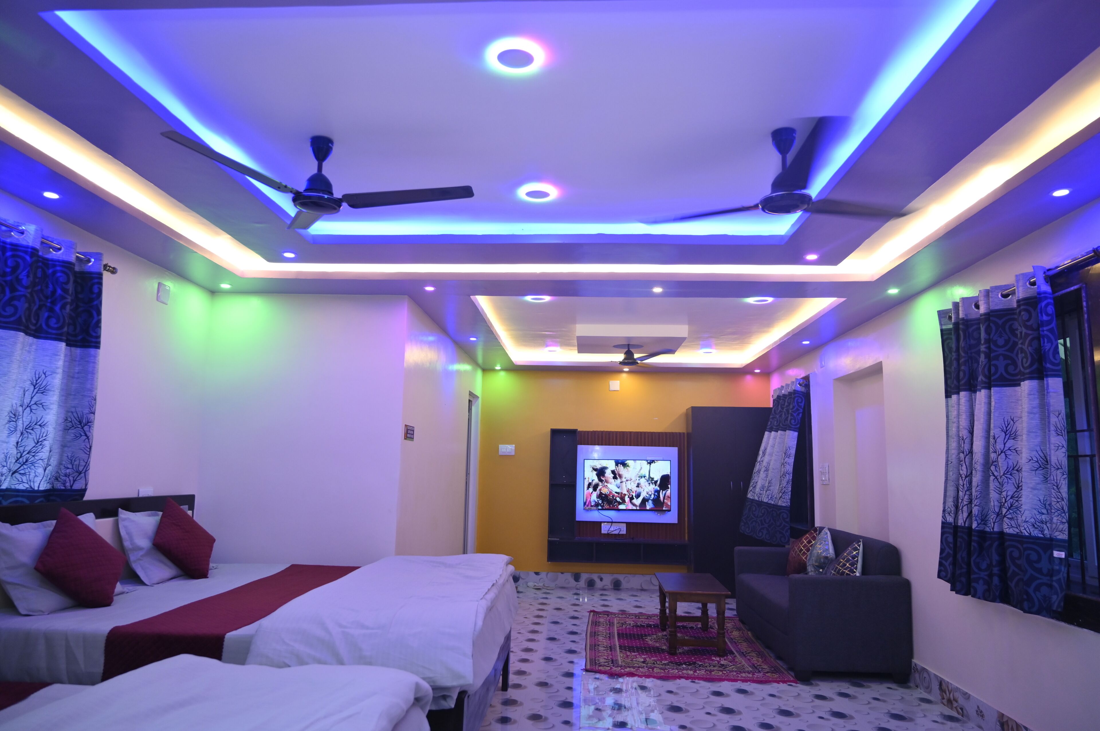 A hotel room with a bed, a sofa, a TV, and ceiling fans.
