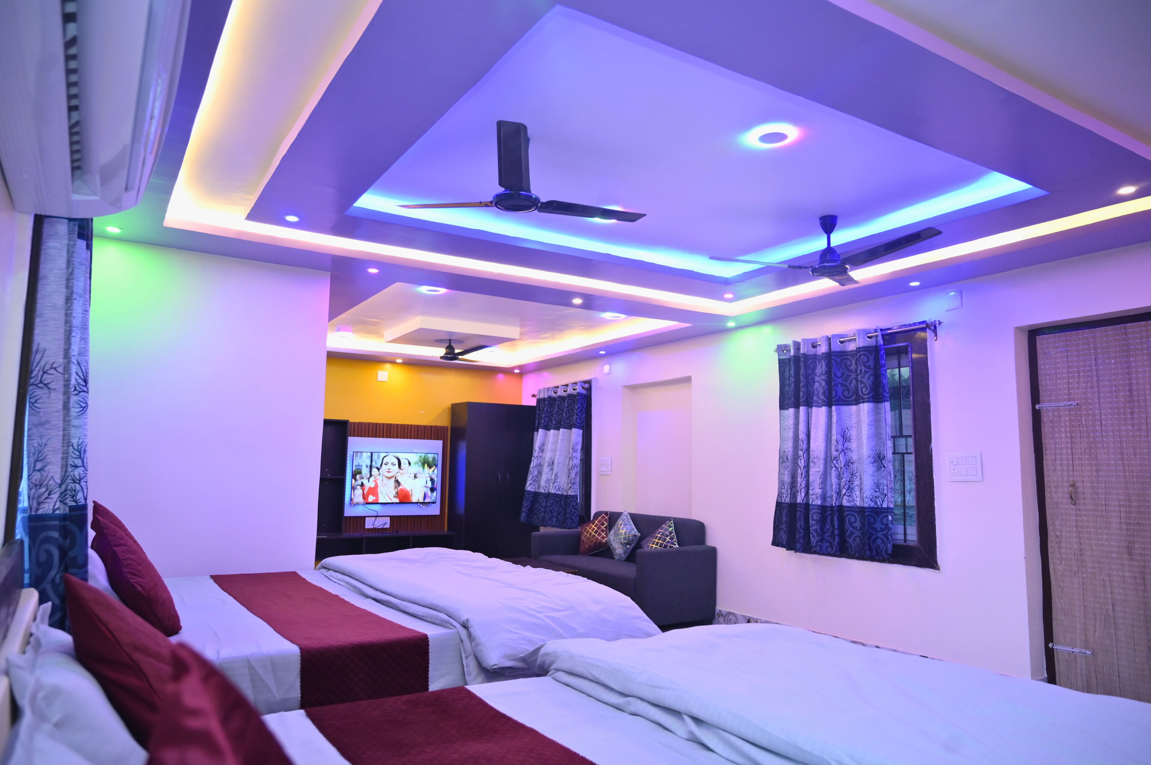 A hotel room with two beds, a TV, ceiling fans, and modern lighting.