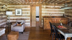 Interno rustico di una baita di legno con zona pranzo, divano, lampada e tavolo in legno con frutta.