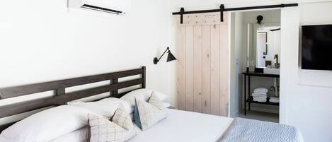 Un dormitorio con cama, aire acondicionado, ventilador de techo, puerta corredera estilo granero, espejo y televisor.