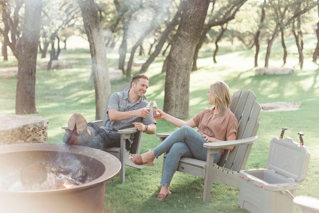 A couple sitting on outdoor patio chairs with a fire pit in the foreground.