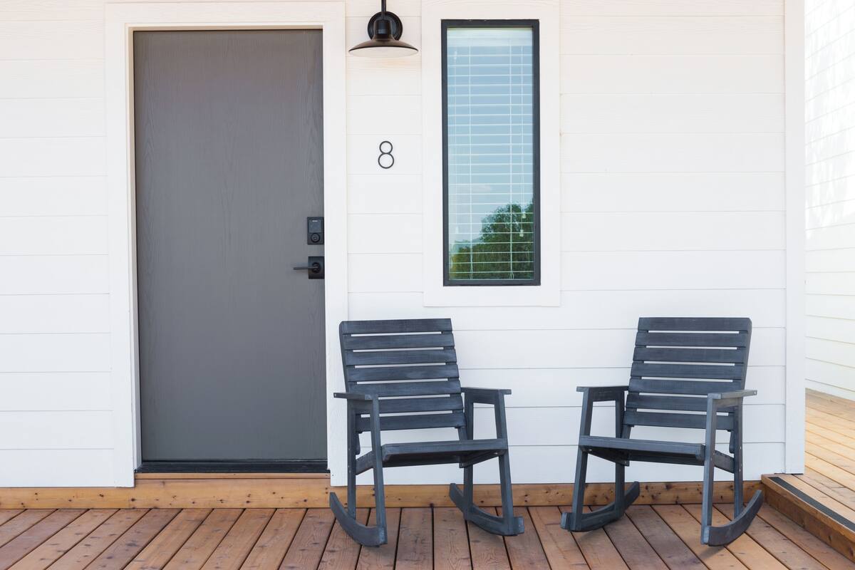 Une terrasse en bois avec deux fauteuils à bascule, une porte grise et une fenêtre sur laquelle est peint le chiffre 8.
