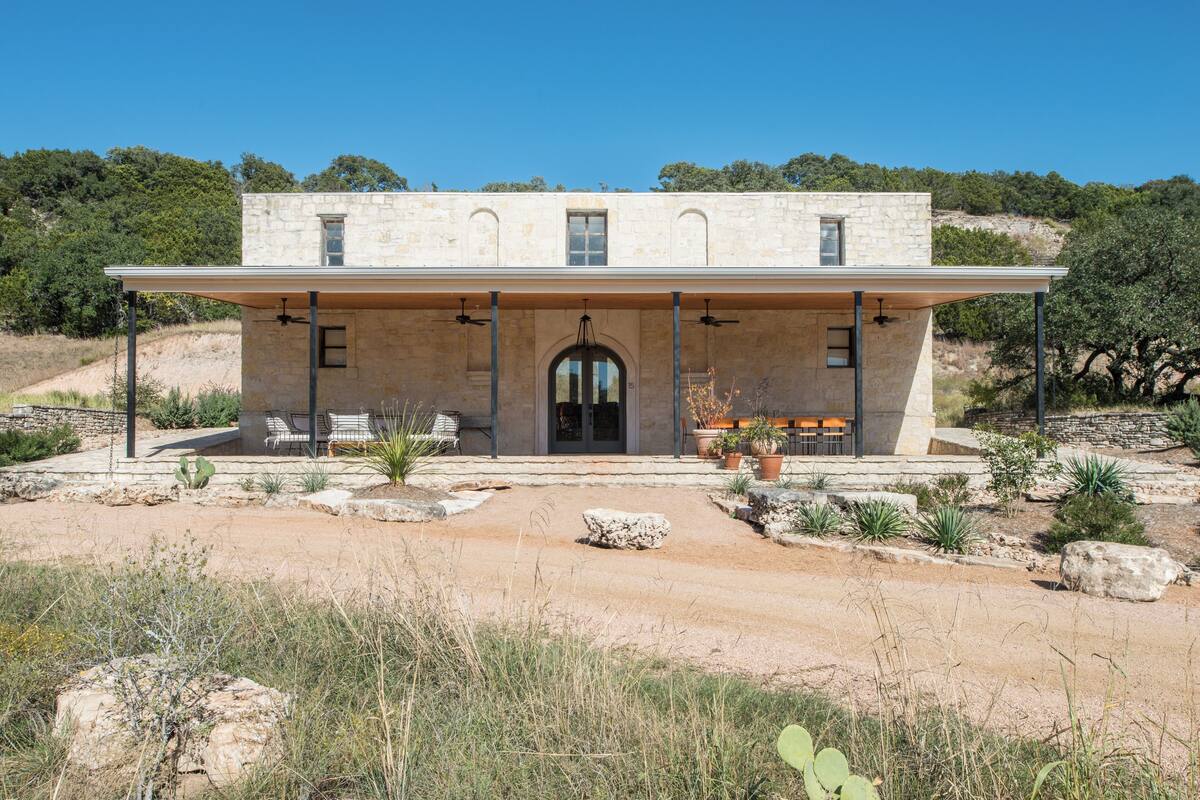 Un bâtiment en pierre de deux étages, doté d’un patio couvert, d’un espace extérieur aménagé et surplombant un paysage désertique.