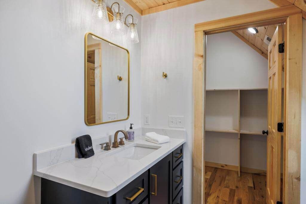 A modern bathroom with a white marble sink, a large mirror, and a wooden ceiling.