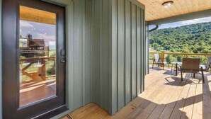 Een houten terras met een deur die uitkomt op een balkon met uitzicht op een bebost glooiend landschap.