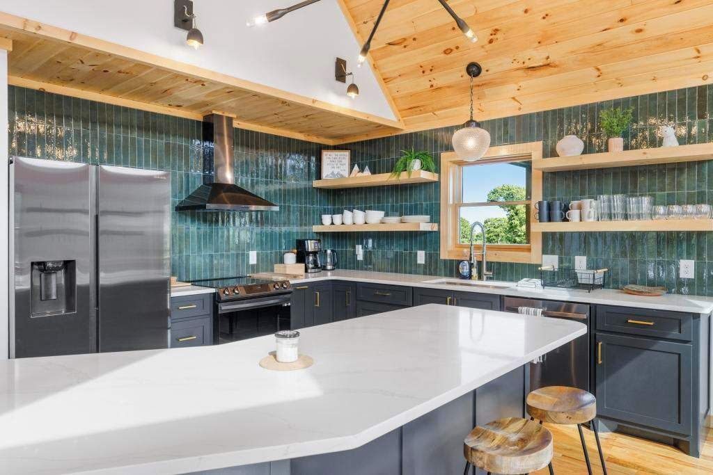 Una cocina moderna con una isla grande, armarios oscuros y techo de madera.