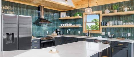 Una cocina moderna con una isla grande, armarios oscuros y techo de madera.