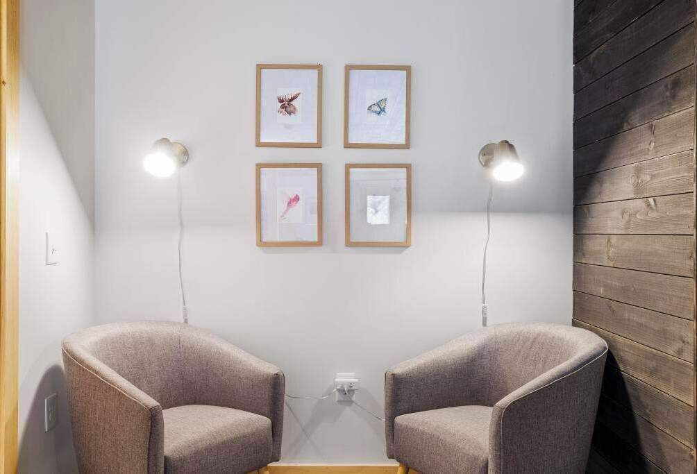 A room with two armchairs, a small table, and four framed pictures on the wall.
