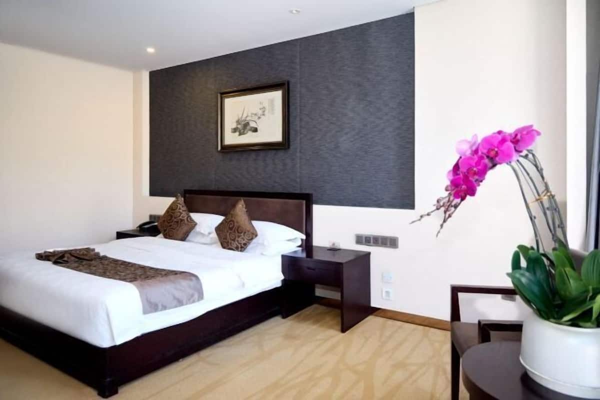 A hotel room with a bed, bedside table, nightstand, and a potted plant.
