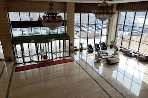 Um lobby amplo com um lustre imponente, divisória de vidro e vista para carros estacionados lá fora.