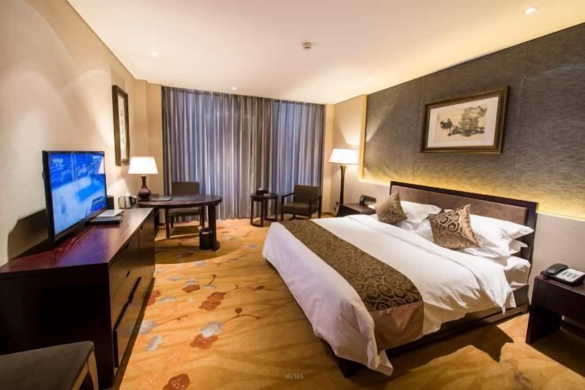 A hotel room with a large bed, a desk with a computer, a TV, and a chair.