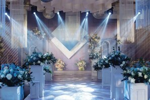 An indoor venue with a stage, floral arrangements, and a patterned floor. - Weichang Qianyue Holiday Hotel (Government Branch) (Weichang)