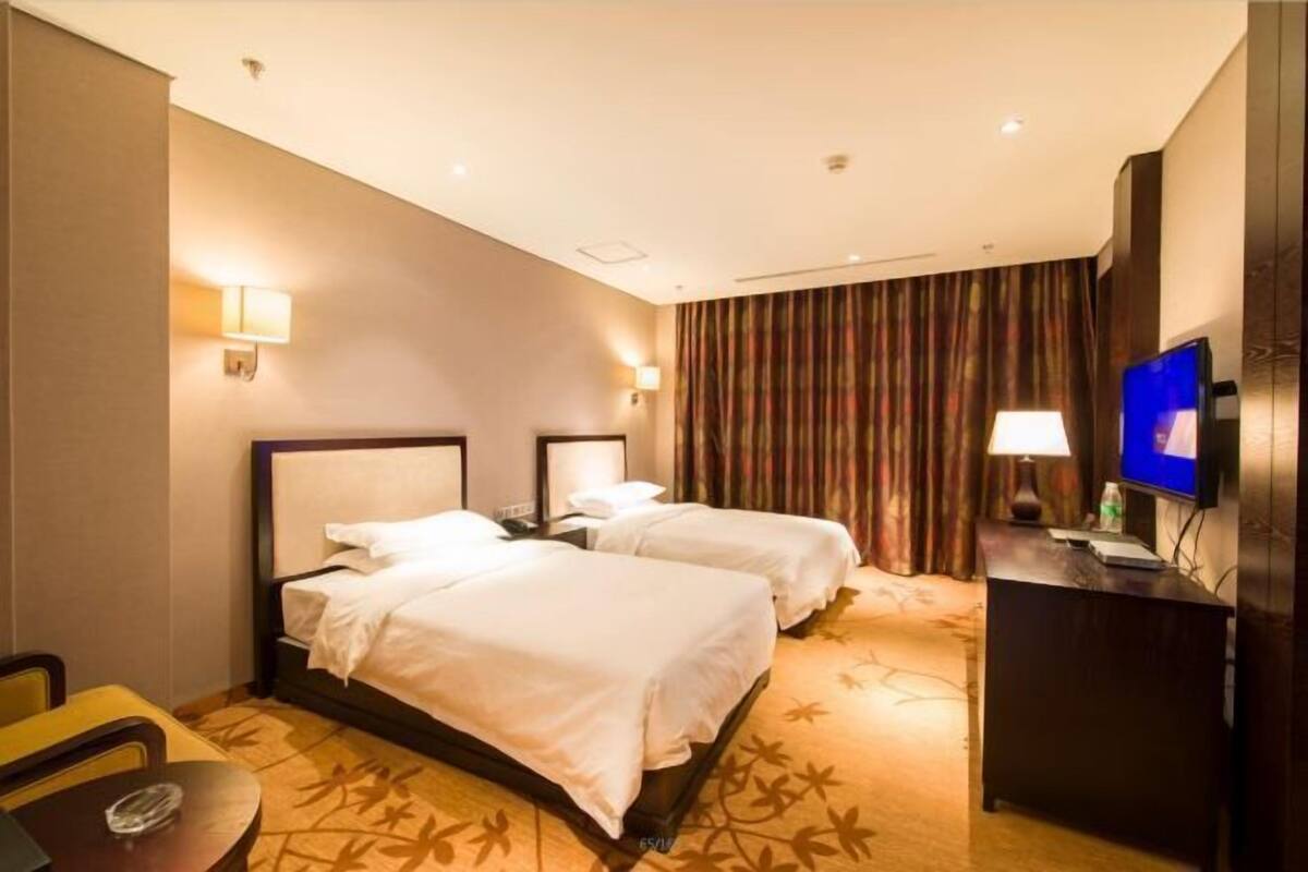 A hotel room with two beds, a desk, a television, and a curtain.