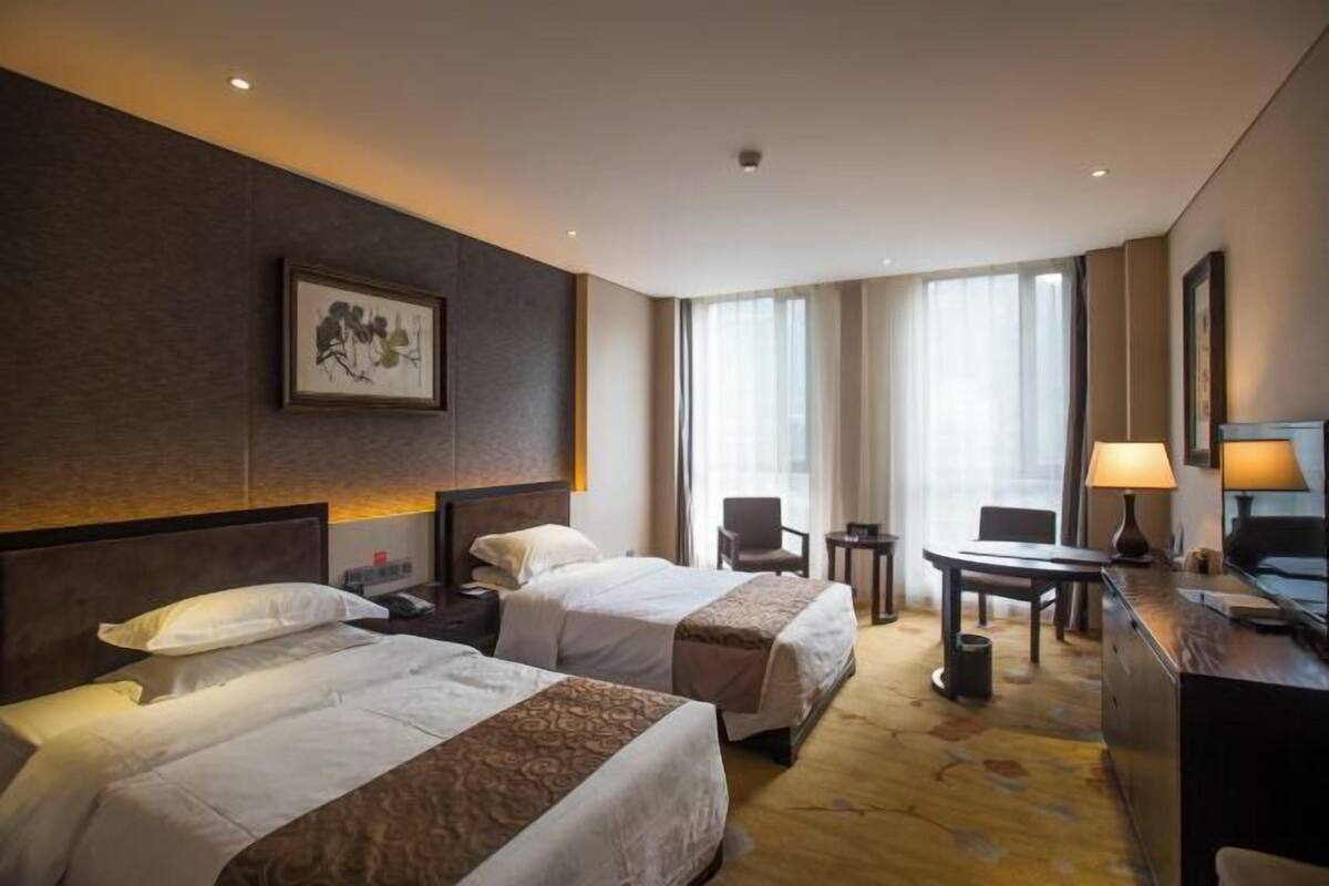 A hotel room with two beds, a desk, a chair, a lamp, and a painting on the wall.