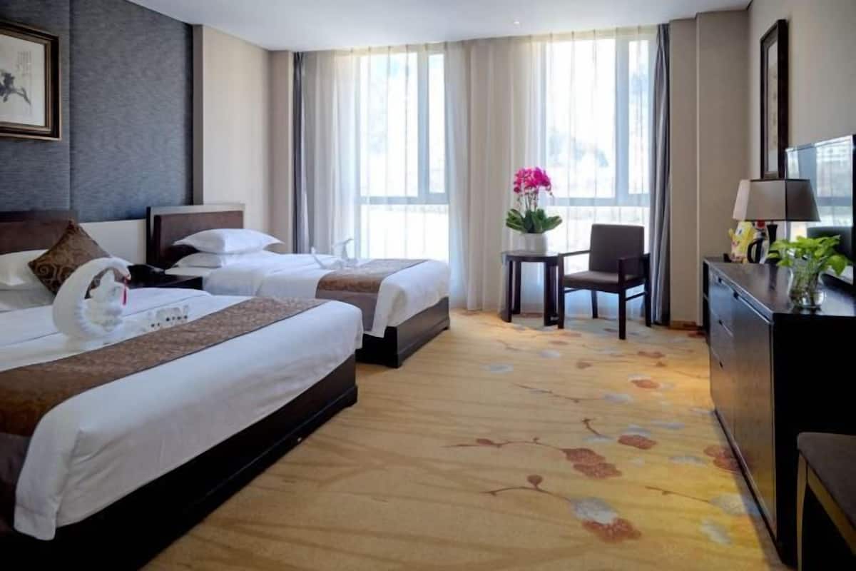 A hotel room with two beds, a desk, a chair, a TV, and a window with curtains.