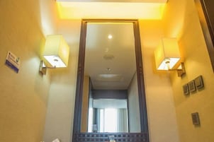 Un pasillo de hotel con un espejo grande, dos lámparas de pared y un suelo de baldosas.