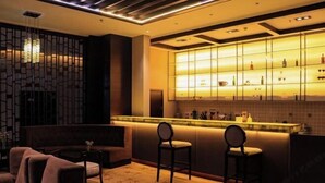 Zona de bar moderna con mostrador, dos taburetes y una pared decorativa con estantes que exhiben botellas y vasos.