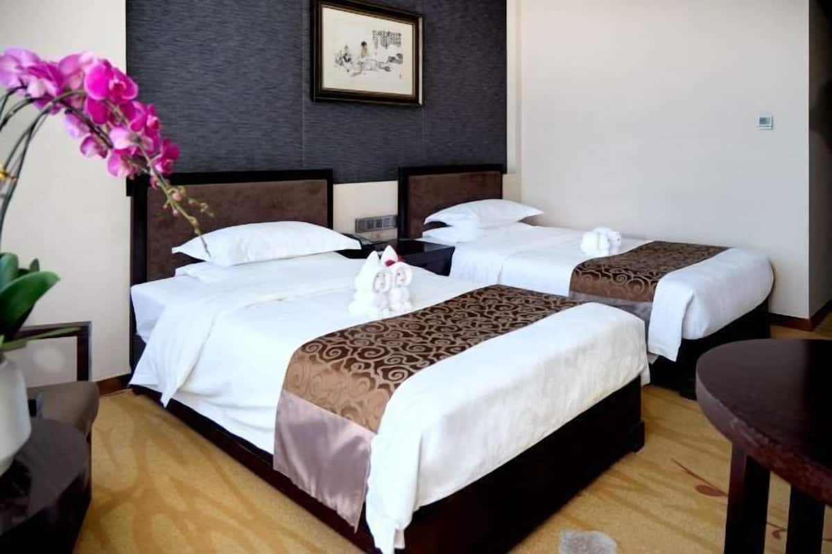 A hotel room with two beds, a bedside table, a small table, and a wall-mounted artwork.