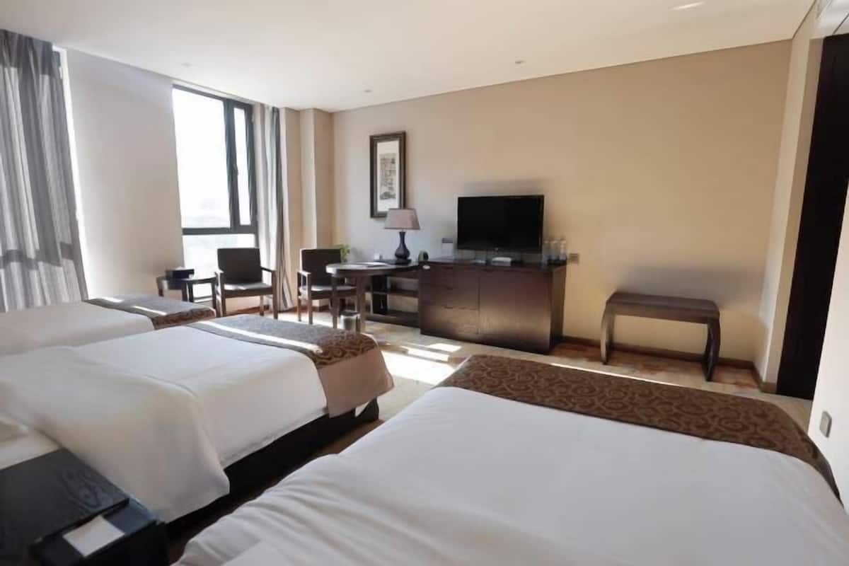 A hotel room with two beds, a desk, a television, and a window.