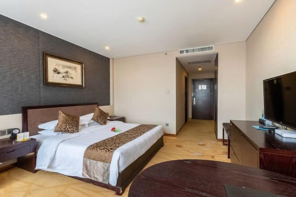 A hotel room with a bed, bedside table, TV, and a desk.
