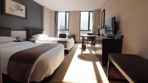 Habitación de hotel con dos camas, un escritorio, un televisor y ventanas amplias.