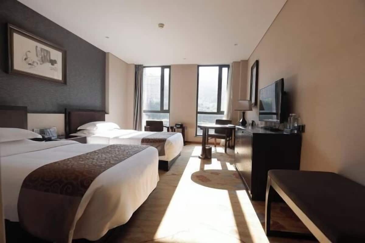 A hotel room with two beds, a desk, a TV, and large windows.