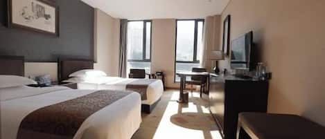 Habitación de hotel con dos camas, un escritorio, un televisor y ventanas amplias.