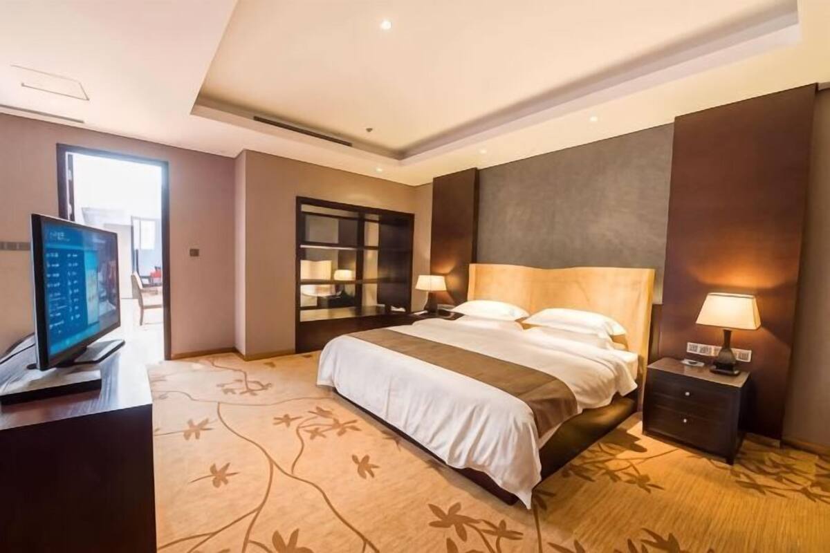 A hotel room with a bed, bedside tables, a TV, and a large window.