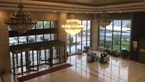 Un vestíbulo amplio con candelabros, una recepción y ventanas grandes con vistas a coches aparcados.
