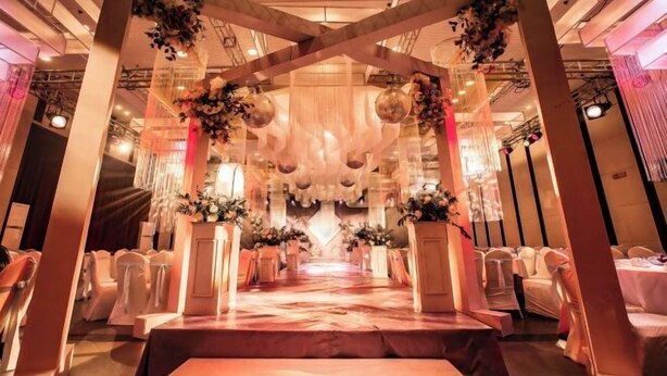 Un salón de banquetes con un pasillo central, sillas blancas a ambos lados y decoración floral.