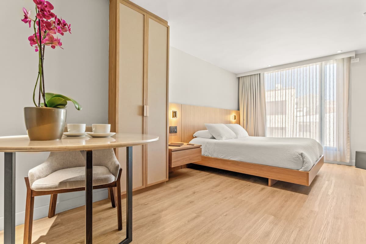 A hotel room with a bed, bedside table, nightstand, and a potted orchid.