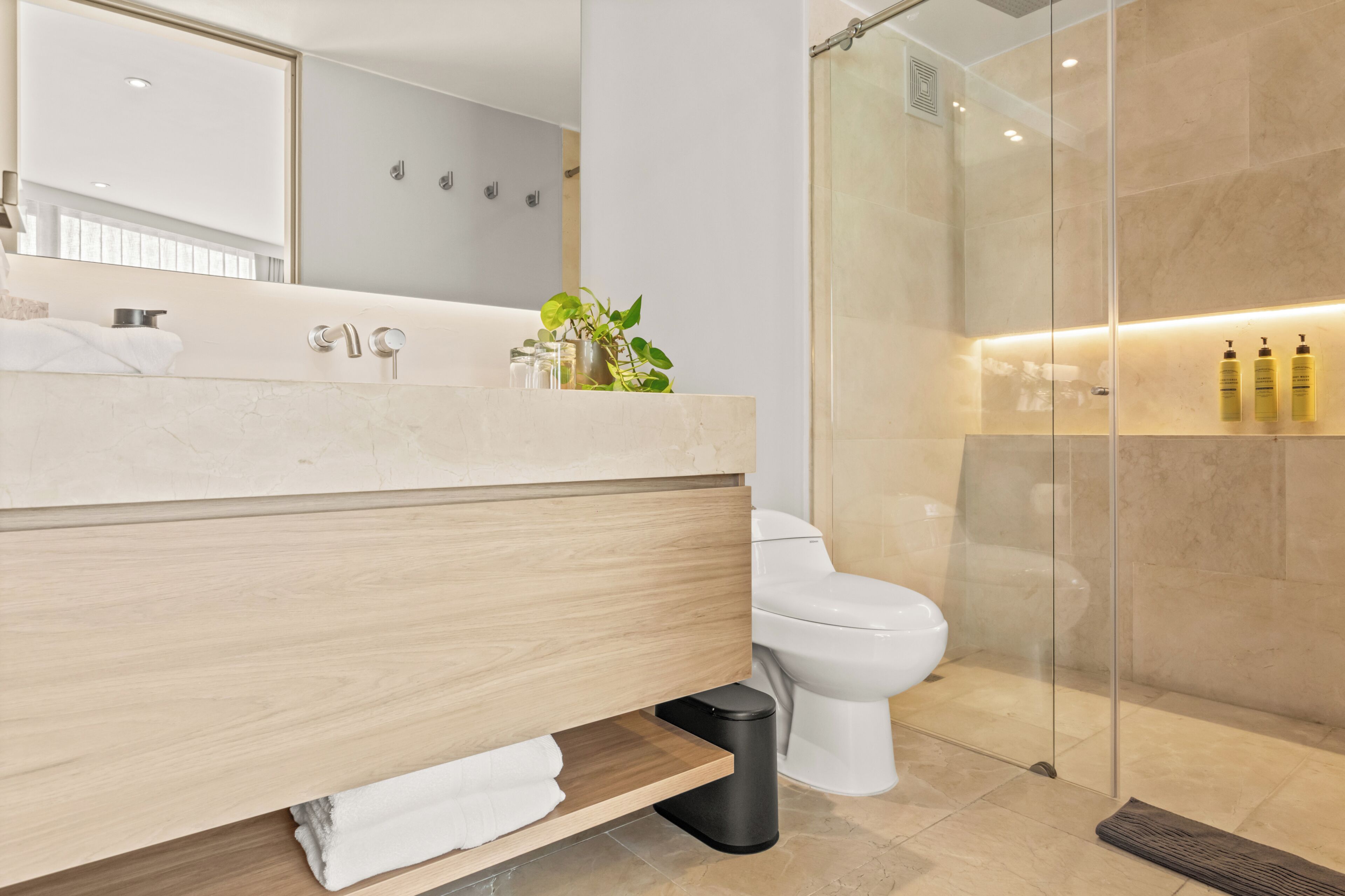 Um banheiro moderno com toucador de madeira, box de vidro e vaso sanitário branco.