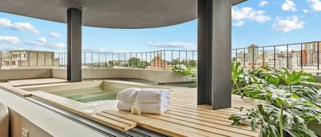 Un área de spa en la azotea con hidromasaje, terraza de madera y plantas en macetas.
