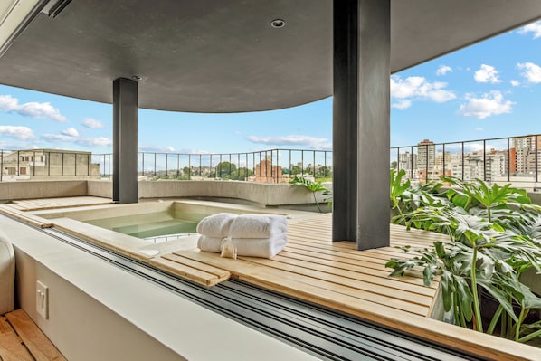 A rooftop spa area with a hot tub, wooden deck, and potted plants.