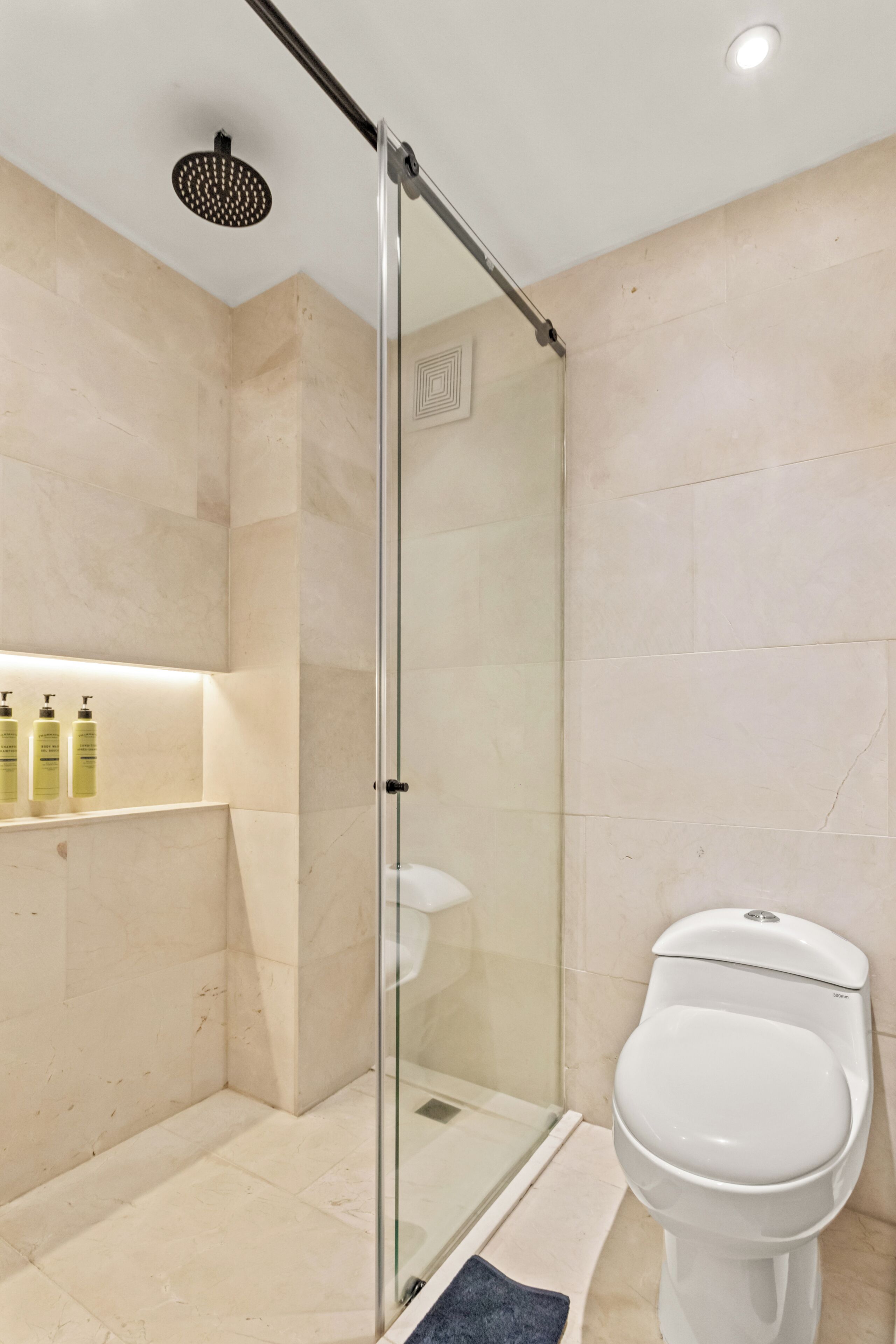 Een moderne badkamer met een glazen douchecabine, een wit toilet en een plank met toiletartikelen.