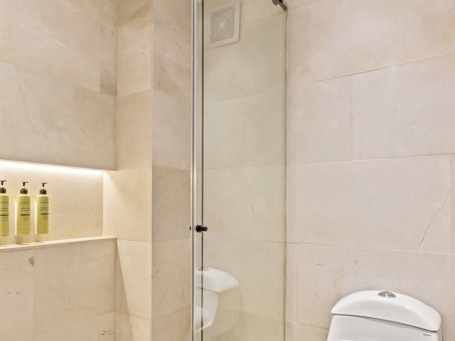 Een moderne badkamer met een glazen douchecabine, een wit toilet en een plank met toiletartikelen.