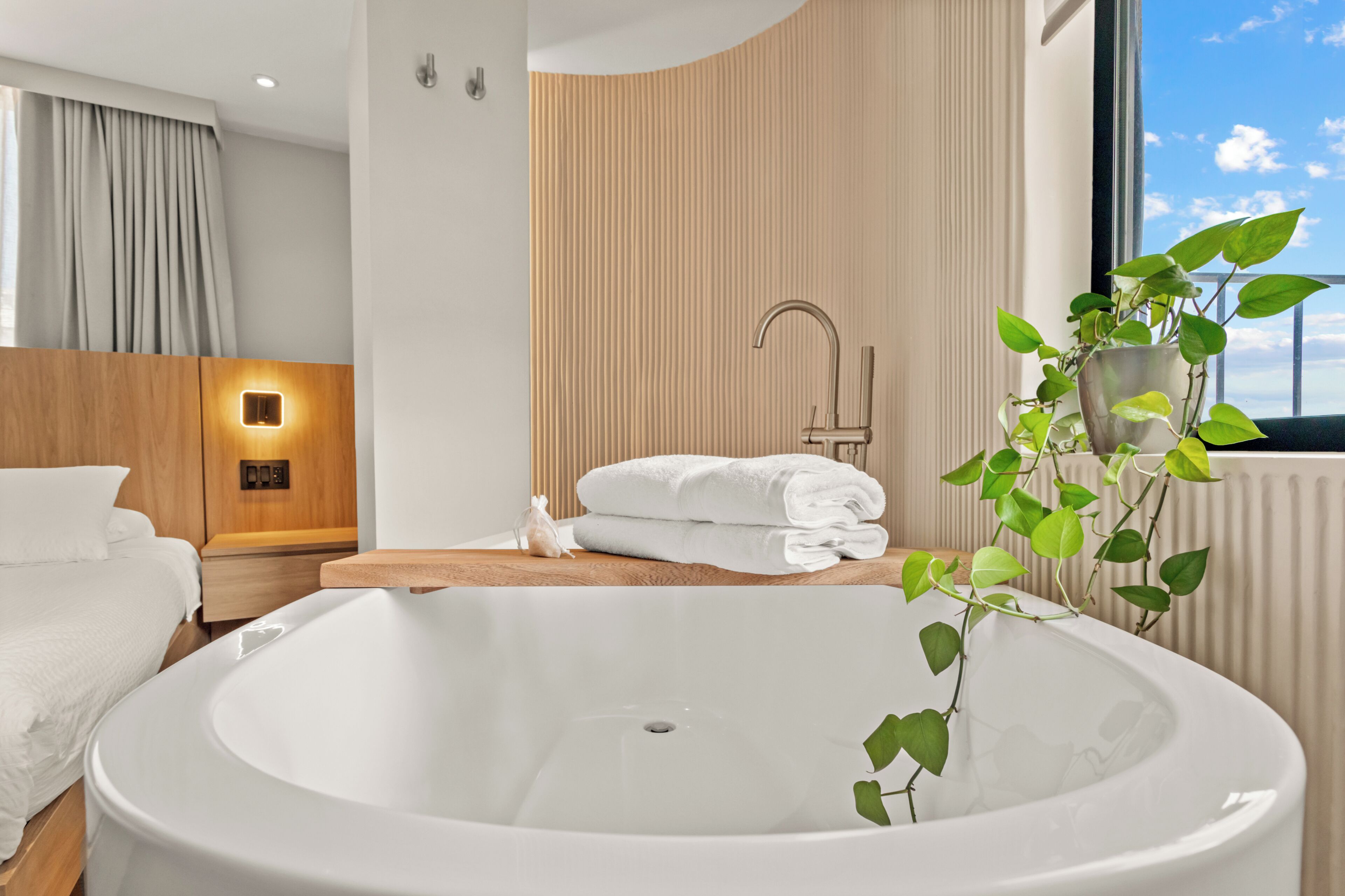 A modern bathroom with a freestanding bathtub, a wooden vanity, a towel rack, and a potted plant.