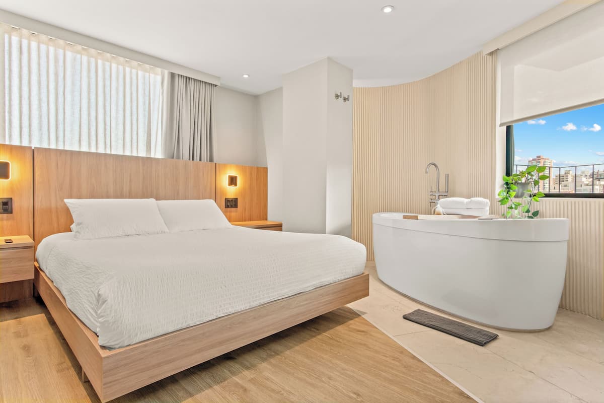 A modern hotel room with a large bed, a built-in bathtub, and a city view.